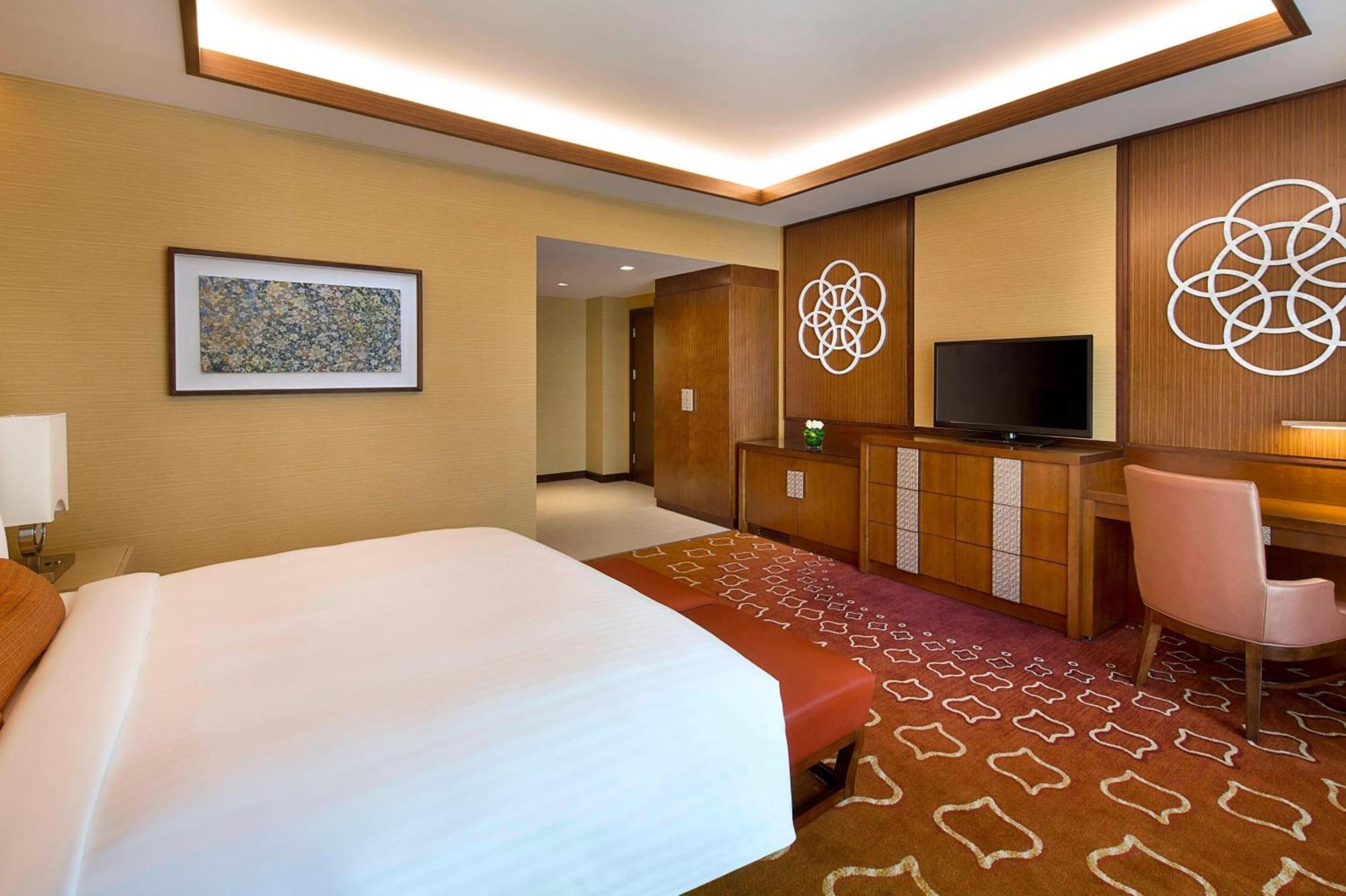 Jabal Omar Marriott Hotel Makkah Mekka Buitenkant foto The photo depicts a modern hotel room featuring a king-sized bed with a white comforter. The room has warm tones, with creamy walls and a patterned carpet in shades of orange. There is a wooden dresser with a flat-screen TV above it. Decorative wall 